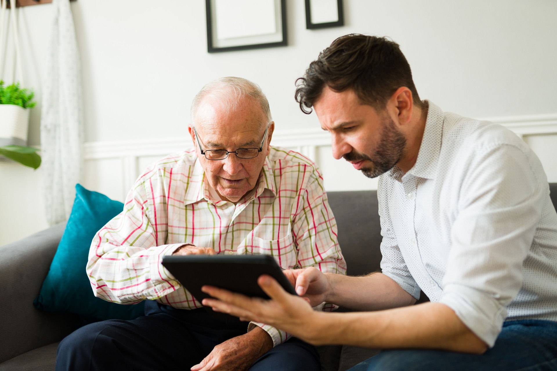 Son helping his senior father to use tablet technology